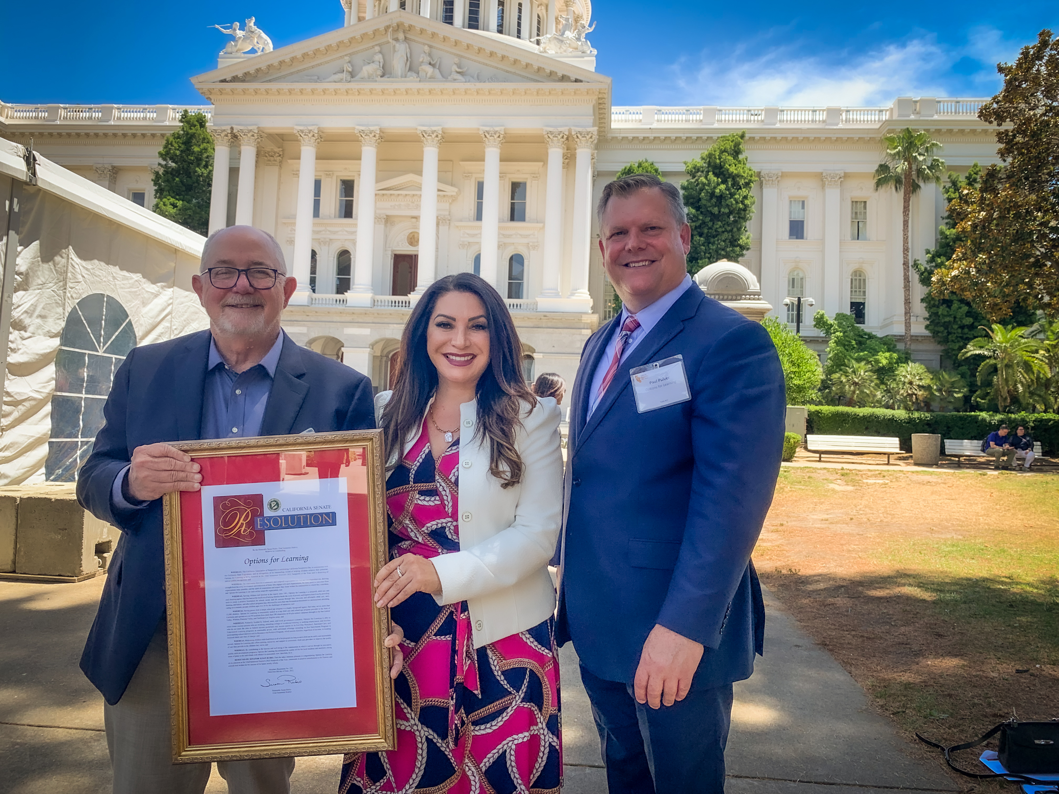 Options for Learning’s board chair, David Wilbur (left), and CEO Paul Pulver (right) accept the state resolution naming the agency a Nonprofit of the Year from Sen. Susan Rubio (center).