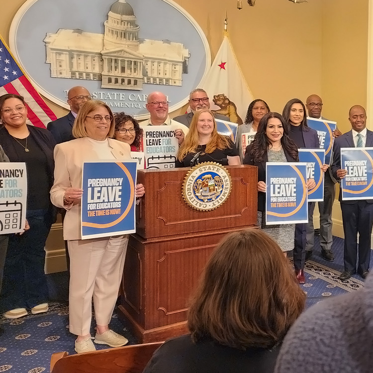 Legislators at a press conference stand in front of the seal of the California State Capitol. Legislators are holding signs for education paid pregnancy leave.