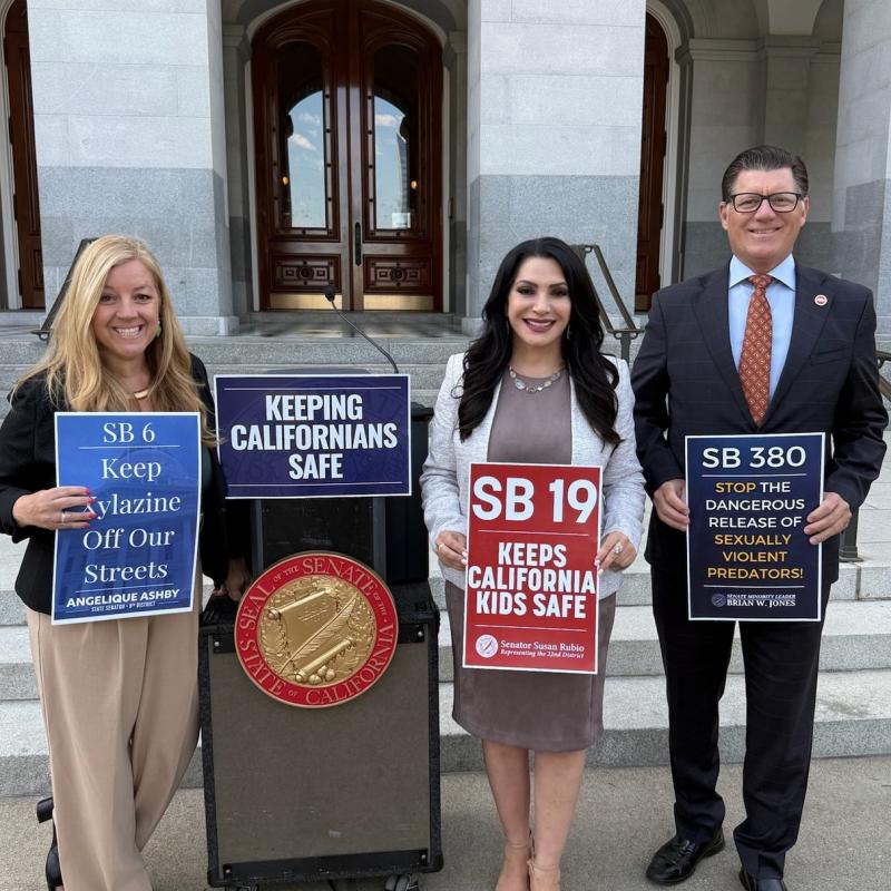 Three senators stand outside the Capitol holding signs for SB 6, SB 19, and SB 380. A podium in front reads “Keeping Californians Safe.”