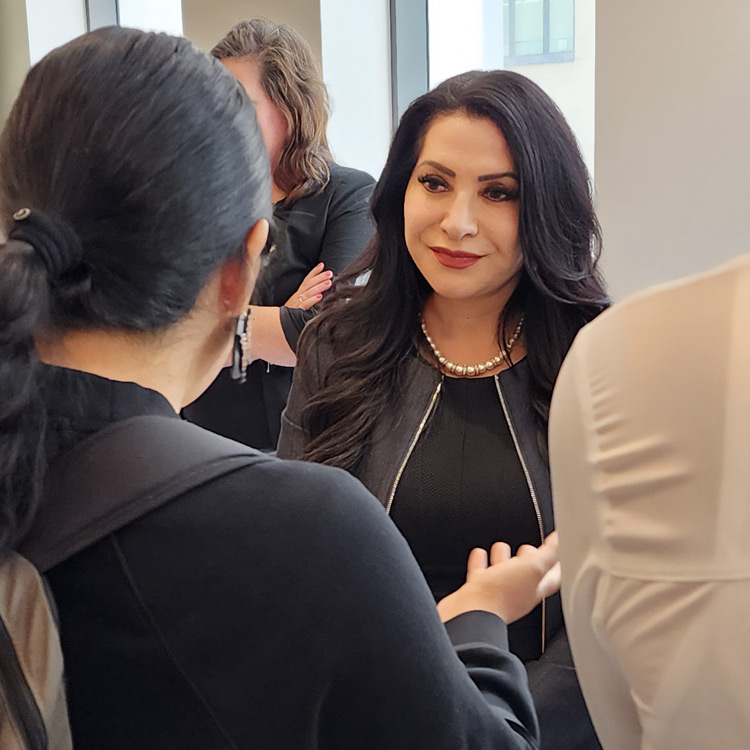 Senator Susan Rubio speaks with committee attendees in the hallway outside the California Senate Education Committee hearing room. She is wearing a black dress and pearl necklace, engaging in conversation with a supporter in the foreground.