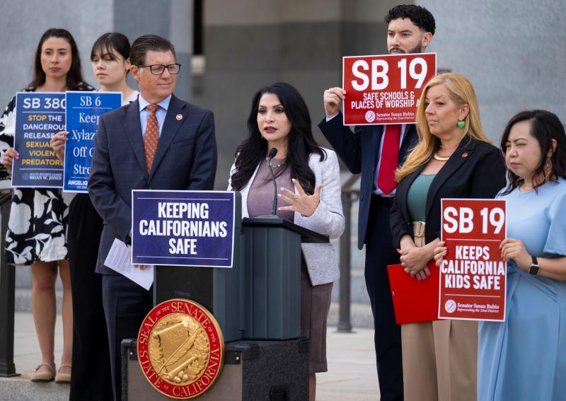 Senator Susan Rubio speaks at a Capitol podium with Senators Angelique Ashby and Brian Jones as supporters hold signs for SB 19 and other bills