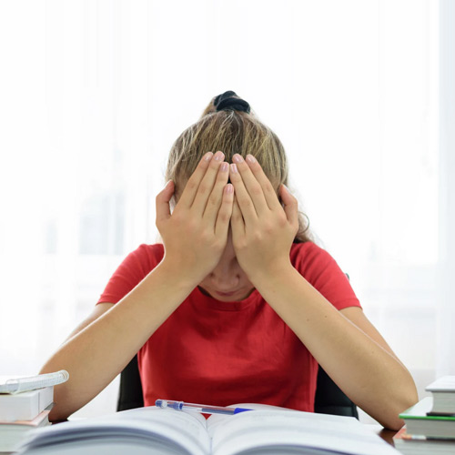 Young female student with her head in her hands while she sits at a table with an open book in front of her